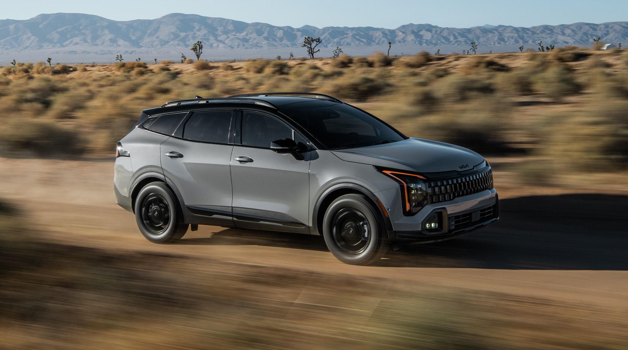 A gray Kia Sportage driving on a dirt road through a desert brush
