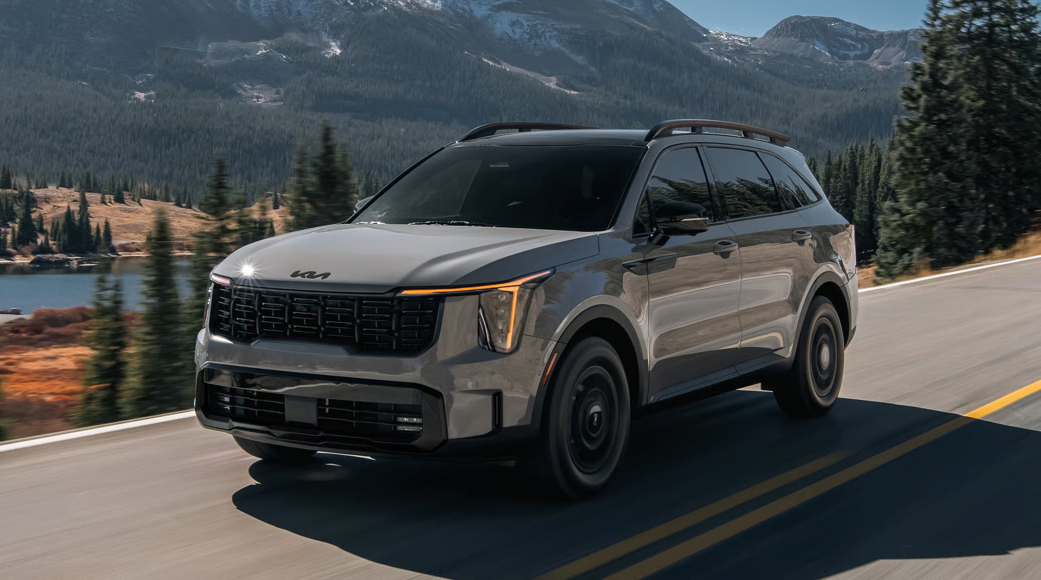 A gray 2027 Kia Sorento SUV driving down a road with mountains in the distance